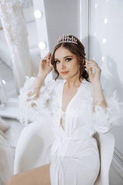 Beyaz bornoz ve taç giyen bir kadın sandalyede oturur. Zarafet ve entelektüellik kavramı. Çünkü kadın resmi bir kıyafet giymiş ve taç takıyor.