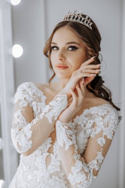 Taçlı ve uzun beyaz elbiseli bir kadın. O bir resim için poz veriyor. Elbise beyaz ve dantelli.