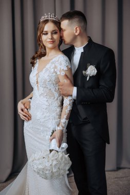 Gelin ve damat fotoğraf için poz veriyor, gelin taç takıyor ve damat takım elbise giyiyor.