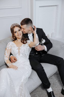 Gelin ve damat kanepede oturuyor, gelin taç takıyor. Sahne romantik ve mutlu.