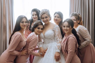 Bir gelin ve nedimeleri resim için poz veriyor. Gelin beyaz bir elbise giyiyor ve nedimeler pembe elbiseler giyiyor. Sahne mutlu ve kutlama dolu, gelin olarak.