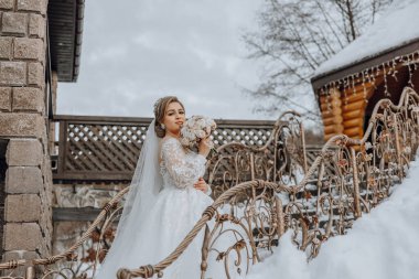 Bir gelin, elinde bir buket çiçek olan bir resim için poz veriyor. Resmin romantik ve zarif bir havası var. Gelin beyaz bir elbise giymiş.