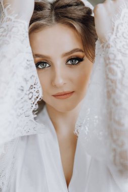 Uzun kahverengi saçlı ve mavi gözlü bir kadın beyaz bir elbise giyiyor. Yüzünde bir gülümsemeyle kameraya bakıyor.