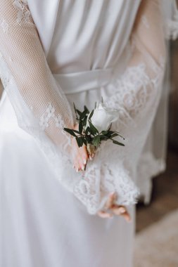 Beyaz bir bornoz giyerken elinde beyaz bir gül tutan bir kadın. Zarafet ve entelektüellik kavramı. Kadın resmi giyinmiş ve elinde narin bir çiçek tutuyor.