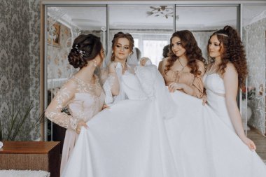 Dört kadın beyaz elbiseli bir fotoğraf için poz veriyor. Elbise çok uzun ve bir sürü ışıltısı var. Kadınların hepsi gülümsüyor ve mutlu görünüyorlar. Sahne neşeli ve kutlayıcıdır.