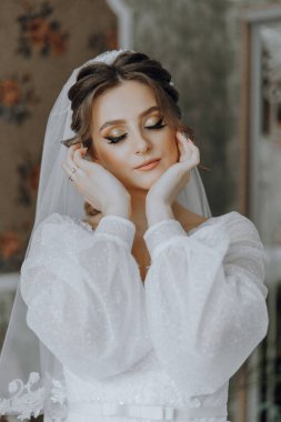 Beyaz elbiseli bir kadın resim için poz veriyor. O bir peçe takıyor ve elleri yüzünde. Şık ve sofistike bir kadın düğün kıyafeti giydiği için.