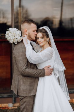 Gelin ve damat resim için poz veriyor, gelin beyaz bir elbise ve damat takım elbise giyiyor.