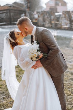 Bir gelin ve damat tarlada öpüşüyor. Gelin beyaz bir elbise giyiyor ve damat da takım elbise giyiyor.