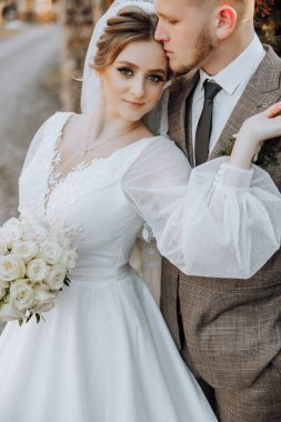 Gelin ve damat resim için poz veriyor, gelin beyaz bir elbise ve damat takım elbise giyiyor.