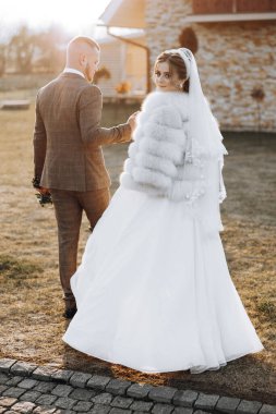 Bir gelin ve damat binanın önündeki patikadan aşağı doğru yürüyorlar. Gelin kürk manto ve peçe giyiyor.