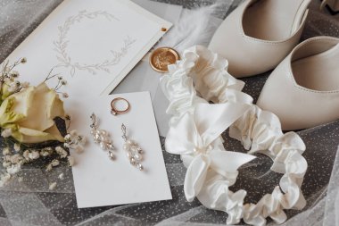 Beyaz dantel bir kurdele beyaz bir kartın üstünde. Kurdelenin sağ tarafında bir çift beyaz ayakkabı var.