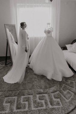 Beyaz elbiseli bir gelin şifoniyerin önünde duruyor. Elbise bir gelinlik.