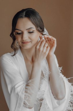 Bir kadın düğün için hazırlanıyor, alyansını ve küpelerini takıyor. Beyaz bir elbise ve beyaz bir şal giyiyor.