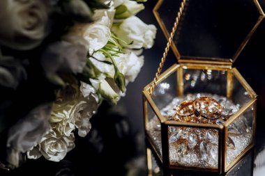 İçinde iki yüzük olan altın ve kristal bir kutu. Kutu bir buket beyaz çiçeğin yanına konur.