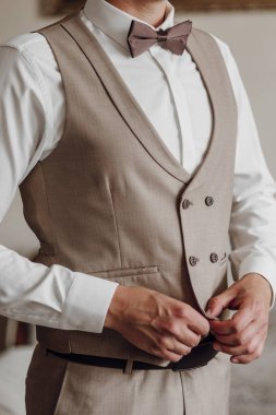 Bronz yelek ve beyaz gömlekli bir adam kravatını düzeltiyor. Formalite ve profesyonellik kavramı. Çünkü adam takım elbise ve kravat giymiş.