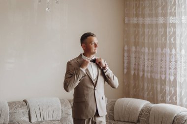 Takım elbiseli bir adam papyonunu bağlamaya hazırlanıyor. Adam takım elbise ve kravat giydiği için resmiyet ve zarafet kavramı. Arka plandaki kanepe biraz rahatlık katıyor