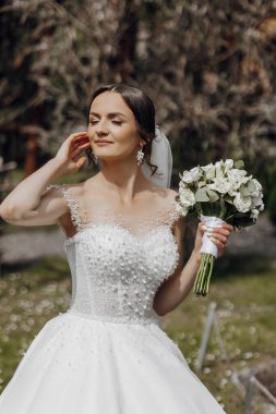 Elinde bir buket çiçek tutan beyaz elbiseli bir kadın. Gülümsüyor ve mutlu.