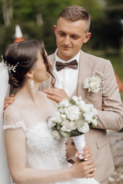 Gelin ve damat birlikte duruyorlar, gelin bir buket tutuyor ve damat takım elbise giyiyor.