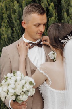 Bir adam bir kadının papyonunu bağlamasına yardım ediyor. Adam takım elbise ve kravat takıyor ve kadın gelinlik giyiyor. Sahne büyük olasılıkla bir düğün ya da resmi bir etkinlikte geçiyor.