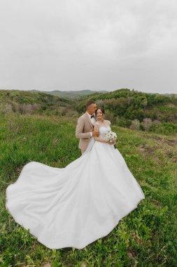 Gelin ve damat bir tarlada, gelinle birlikte uzun beyaz bir elbise giyiyorlar. Gelin bir buket çiçek tutuyor ve damat onu yanağından öpüyor. Sahne çok romantik.