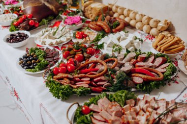 Bir masa çeşitli et, sebze ve ekmekle kaplıdır. Masa büyük bir toplantı için hazırlandı ve yemekler görsel olarak çekici ve davetkar bir şekilde düzenlendi.