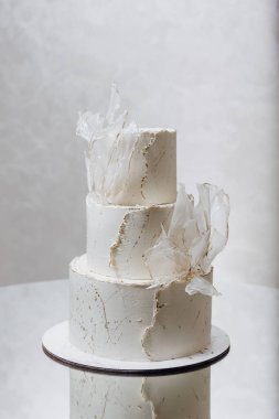 Üç katlı beyaz pasta, beyaz kremalı ve beyaz yapraklı süslemeli. Pasta masaya konur.