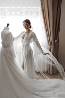 Bir kadın gelinlik sergisinin önünde duruyor. Beyaz bir elbise giyiyor ve bir resim için poz veriyor.