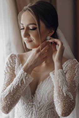 Bir kadın kulaklarını deldiriyor. Gelinlik giyiyor ve saçları topuz şeklinde.