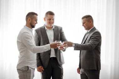 Takım elbiseli üç adam bir kadeh şarapla birbirlerine kadeh kaldırıyorlar. Sahne kutlama ve dostça