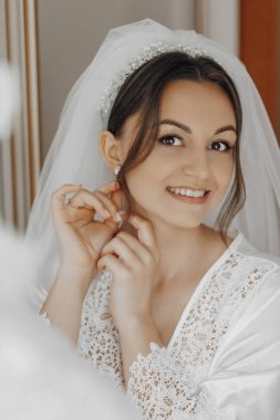 Bir gelin düğünü için hazırlanıyor ve duvağını takıyor. Gülümsüyor ve kameraya bakıyor.