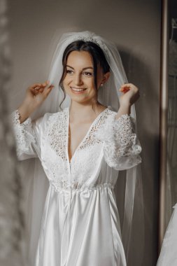 Beyaz elbiseli bir kadın gülümsüyor ve duvağını düzeltiyor. Mutluluk ve kutlama kavramı. Kadın özel bir olaya hazırlanıyor. Düğün ya da resmi bir etkinlik gibi.