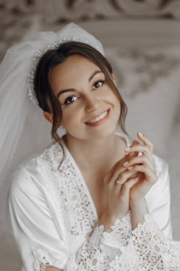 Bir kadın gülümsüyor ve dantelli beyaz bir elbise giyiyor. O bir resim için poz veriyor. İmajın mutlu ve romantik bir havası var.