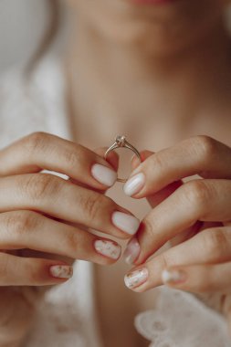 Bir kadın elinde bir yüzük tutuyor. Kadın beyaz bir elbise giyiyor ve elleri birbirine kenetlenmiş. Aşk ve bağlılık kavramı