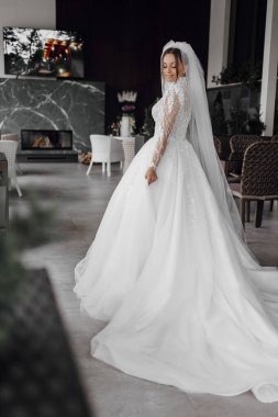 Uzun beyaz elbiseli bir gelin şöminenin önünde duruyor.