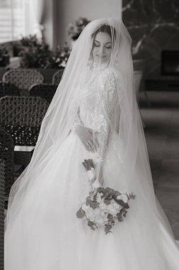 Beyaz bir elbise ve duvak takan bir gelin. Elinde bir buket çiçek tutuyor.