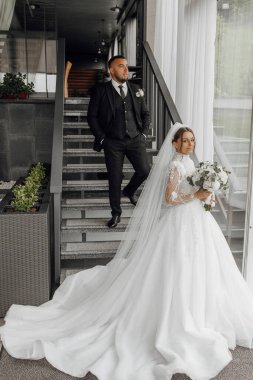 Gelin ve damat bir merdivende, gelin bir buket çiçek tutuyor. Aşk ve mutluluk kavramı, çift evlenirken. Gelinin elbisesi uzun ve zarif.