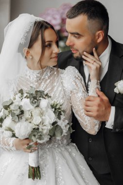 Gelin ve damat, gelinin elinde bir buket çiçekle poz veriyorlar.