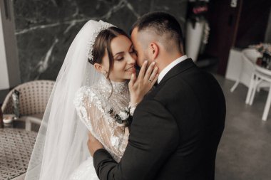 Bir gelin ve damat birbirlerine siyah takım elbise ve beyaz peçeyle sarılıyorlar.