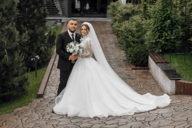 Gelin ve damat tuğla bir geçidin önünde duruyorlar, gelin bir buket tutuyor ve damat kravat takıyor.