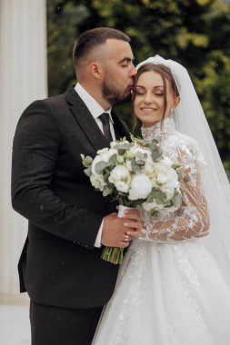 Bir erkek bir buket çiçek tutarken bir kadının yanağını öper. Çift resmi giysiler giyiyor ve sahne bir kilisede geçiyor. Sahne romantik ve samimi.