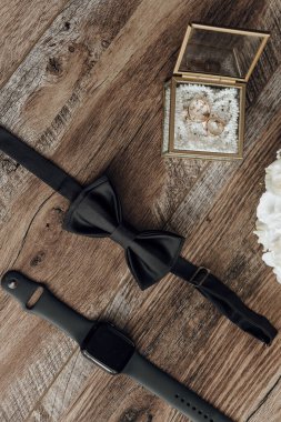 Siyah bir kravat, içinde iki yüzük olan altın bir kutunun yanındaki ahşap bir masada. Kravat bir saat ve bir çift küpenin yanında. Sahne zarif ve sofistike.