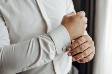 Bir adam beyaz gömlek giyiyor ve manşetlerini düzeltiyor. Formalite ve detaylara dikkat etme kavramı. Çünkü adam düzgün giyinmeye özen gösteriyor.