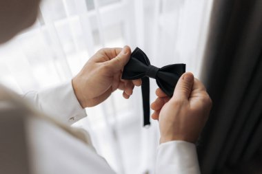 Bir adam papyonunu bağlamaya hazırlanıyor. O, kravatı elinde tutuyor ve ayarlıyor. Hazırlık kavramı ve detaylara dikkat