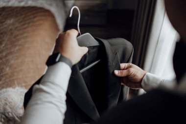 Siyah ceketini asan bir adam var. Adam saat takıyor ve ceketi omuzlarından tutuyor.