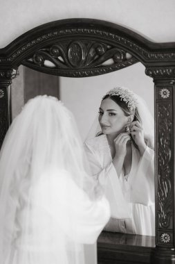 Bir kadın düğün için hazırlanıyor ve aynada kendine bakıyor. Duvak ve başlık takıyor.