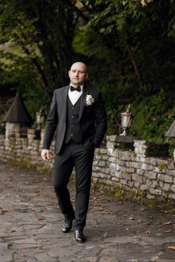 Takım elbiseli ve kravatlı bir adam yakasında beyaz bir çiçekle yolda yürüyor.