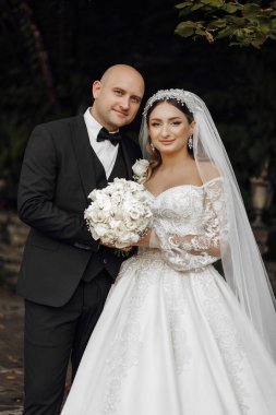 Bir gelin ve damat bir buket beyaz çiçekli bir resim için poz veriyorlar. Gelin uzun beyaz bir elbise giyiyor ve damat bir takım elbise giyiyor. Sahne mutlu ve kutlama dolu.