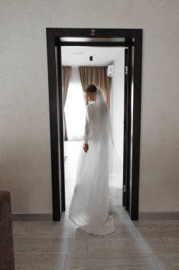 Beyaz bir elbise ve duvak takmış bir gelin kapının önünde duruyor. Gelin çerçevede görünen tek kişi olduğu için, imajın dengesiz ve dramatik bir havası var. Kapı kapalı gibi görünüyor.