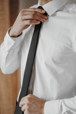 Bir adam kravatını bağlamaya hazırlanıyor. Beyaz gömlek ve siyah kravat giyiyor.
