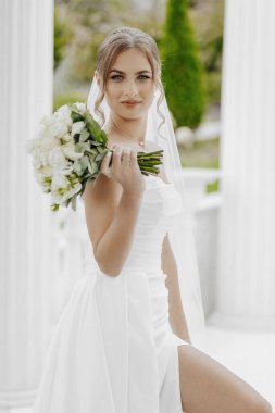 Elinde bir buket çiçek tutan beyaz elbiseli bir kadın. O bir düğün duvağı ve parmağında bir yüzük takıyor. İmajın romantik ve zarif bir havası var.